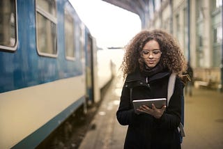 A young woman on a railway station, looking at her iPad.