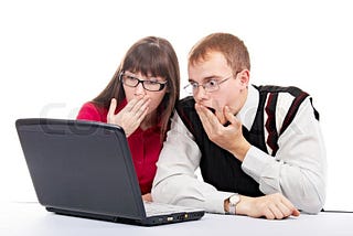 Two very scared people look at a laptop.