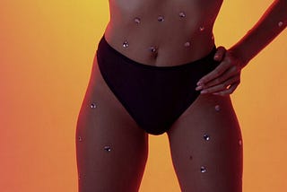 A woman in a bikini with silver studs on her body, looking glamorous on the beach.