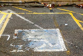 Imagem de vaga de estacionamento reservada para pessoa com cadeira de rodas. A pintura do simbolo da cadeira de rodas está desgastada.