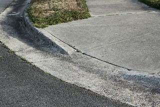 Picture of a curb cut, showing part of the street and a gentle slope onto the sidewalk.
