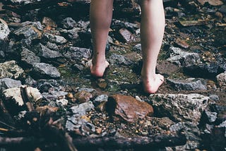 Woman standing barefoot on rocks with water flowing past.
