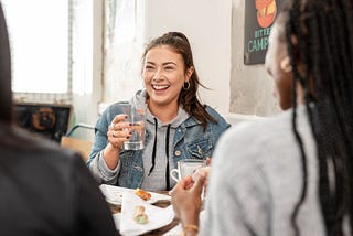 A student is smiling while speaking to friends — they are eating and drinking.