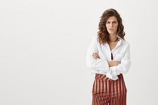 Middle-aged woman wearing a white shirt and stripey trousers looking mad.