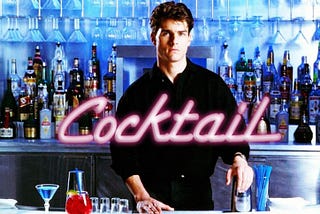 Still of Tom Cruise in film “Cocktail,” standing behind bar with wall of various liquor bottles and glasses behind him and film title in neon pink font superimposed in front center.