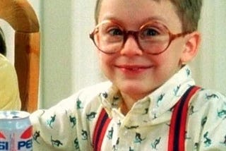 little boy with glasses grins while drinking from a can of Pepsi