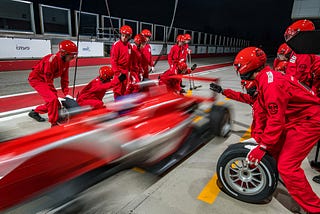 Image of a Formula One pit crew swiftly replacing a tire on a red Formula One car, symbolizing how Scrum of Scrums meetings streamline collaboration among cross-functional teams in Agile project management.