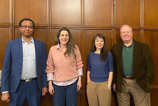 Four speakers standing against a brown paneled wall.