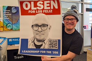 Olsen Ebright holds a campaign poster as part of his 2025 LFNC re-election bid in this photo taken at the FedEx Office Print & Ship Center located near the intersection of Sunset Boulevard and Western Avenue in Los Angeles.