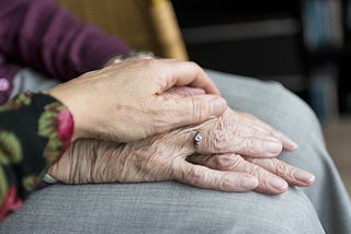 A woman’s hand covers the wrinkled hand of her elderly mother.