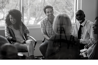 A diverse looking group of people sitting in a circle, apparently in an office setting.