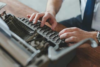 A man’s hands typing on an old typewriter.