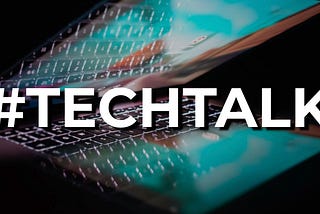 #TECHTALK hashtag in large bold white text with offset shadow over a dark photo of a half open laptop with the screen on with bright blue reflecting some of the keys