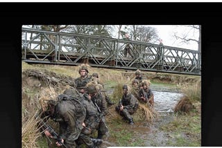 Soldiers on exercise crawling through a stream in camouflage gear