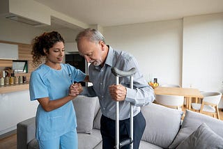 Home health aide helps an old man on a crutch