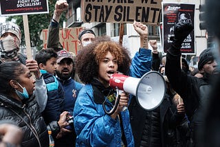 Image of protesters during Black Lives Matter. People are holding signs and the person at the centre of the image is holding a loud speaker.