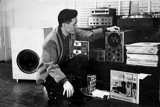 A man crouching down while looking at analog stereos and vinyl records