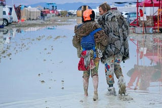 A couple seen from behind gaze at an expanse of flooded field while wading in mud.