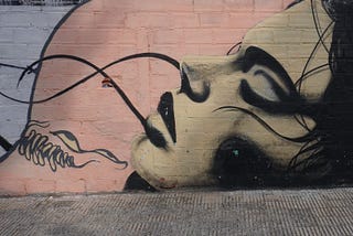 Graffiti art depicting a woman with eyes closed lying next to a monstrous creature baring sharp teeth and menacing eyes