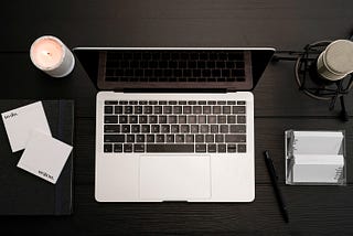 Macbook, sticky notes, microphone and a burning candle on a black desk