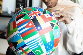 A female in a headscarf is holding and looking at a globe with illustrations of the different flags of many countries.