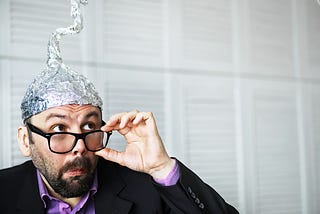 Man with glasses, a beard and a tin foil hat.