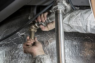 Photo of a worker’s hands fixing plumbing against a gray background.