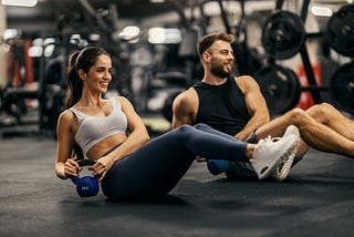 Two people, performing a core workout on the gym floor.