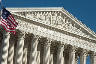 The U.S. Supreme Court building in Washington, DC, with an American flag. The text carved across the building’s face reads: Equal Justice Under Law