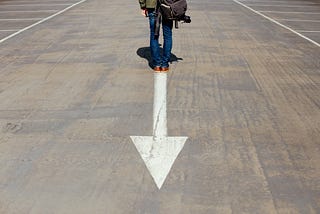 Man standing on arrow sign (photo by Smart on Unsplash)