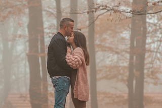 Couple in layered clothing in fall woods.