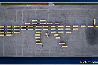 fifty two yellow schools buses arranged in the shape of an AR-15 assault weapon; one bus represents the trigger, and another represents the front sight