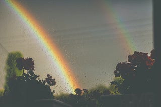 a double rainbow is shown across a rainy sky