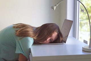 A bored girl lying on a her laptop on a white desk on a sunny morning