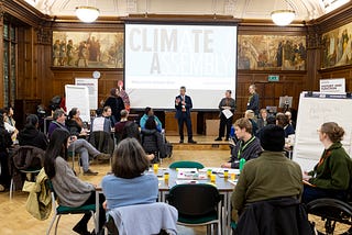 People on tables surrounding a speaker in a large wood panelled room