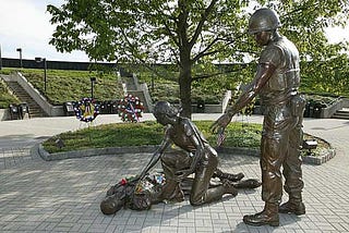 a bronze statue of a nurse and a soldier leaning over a wounded soldier on the ground — Vietnam veterans benefits