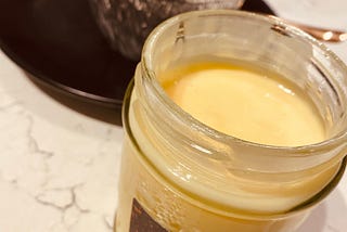 A glass jar that contains custard on it on the front and faintly visible on the back a crumble served on a tin foil plate.