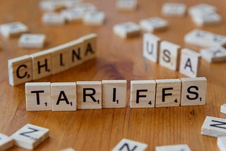 Scrabble tiles standing on edge, spelling out TARIFFS, CHINA, and USA.