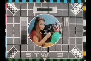 Channel 9 test pattern from the 1970’s, showing a test pattern with a girl holding chalk playing noughts and crosses, next to a clown doll.