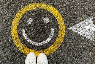 Person’s feet standing next to a smiley face stenciled on the pavement.