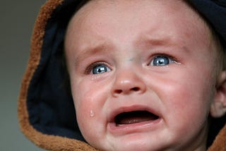 A close-up of a crying baby face with big blue tear filled eyes.