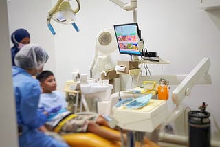 A child, dentist, and nurse. The child is seating on a dental chair.