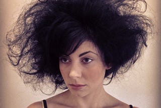 A woman messy black hairstyle, wearing a black tank top against a plain background.
