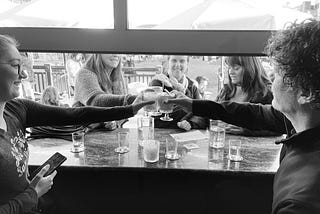 Five people toasting drinks across an open window