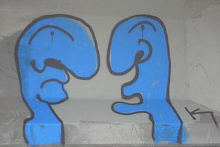 Two blue figures painted on a wall in dicussion.