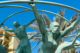 A dramatic bronze statue of men reaching for the outer limits of a circle