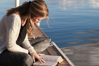 A woman sits on a dock, reading a book.