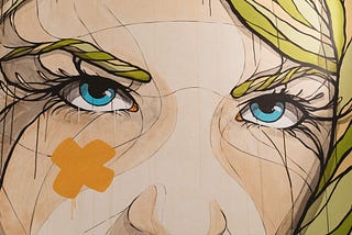 Graffiti art of blonde woman with blue eyes with an orange x on left cheek