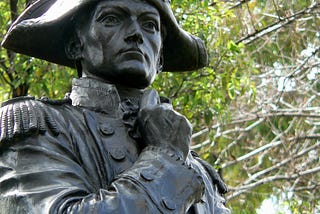 Closeup, bronze statue, Flinders with pensive look on his face, right arm raised selfconsciously to his chest