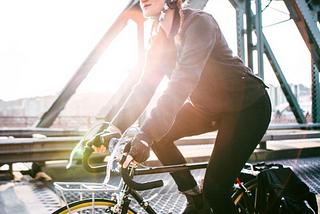 a woman rides a bike over a metal bridge. the sun is shining brightly